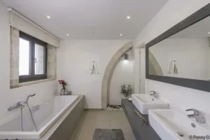 En-suite bathroom at Villa Levanda with a bath, twin basins and a stone arch